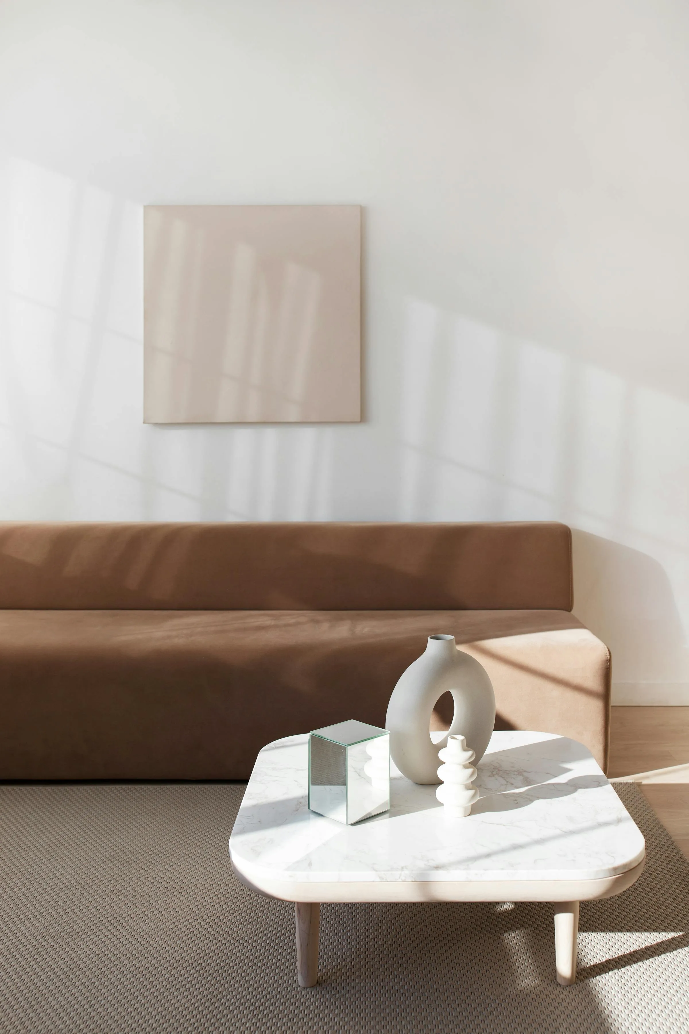 A calm, light-filled room with a warm sofa and softly illuminated still life.